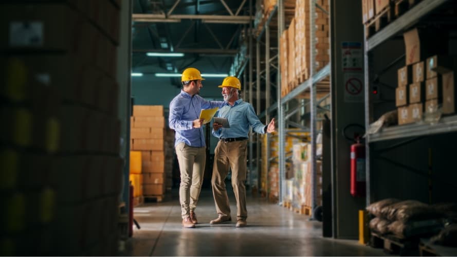 Two people walking in warehouse discussing business.